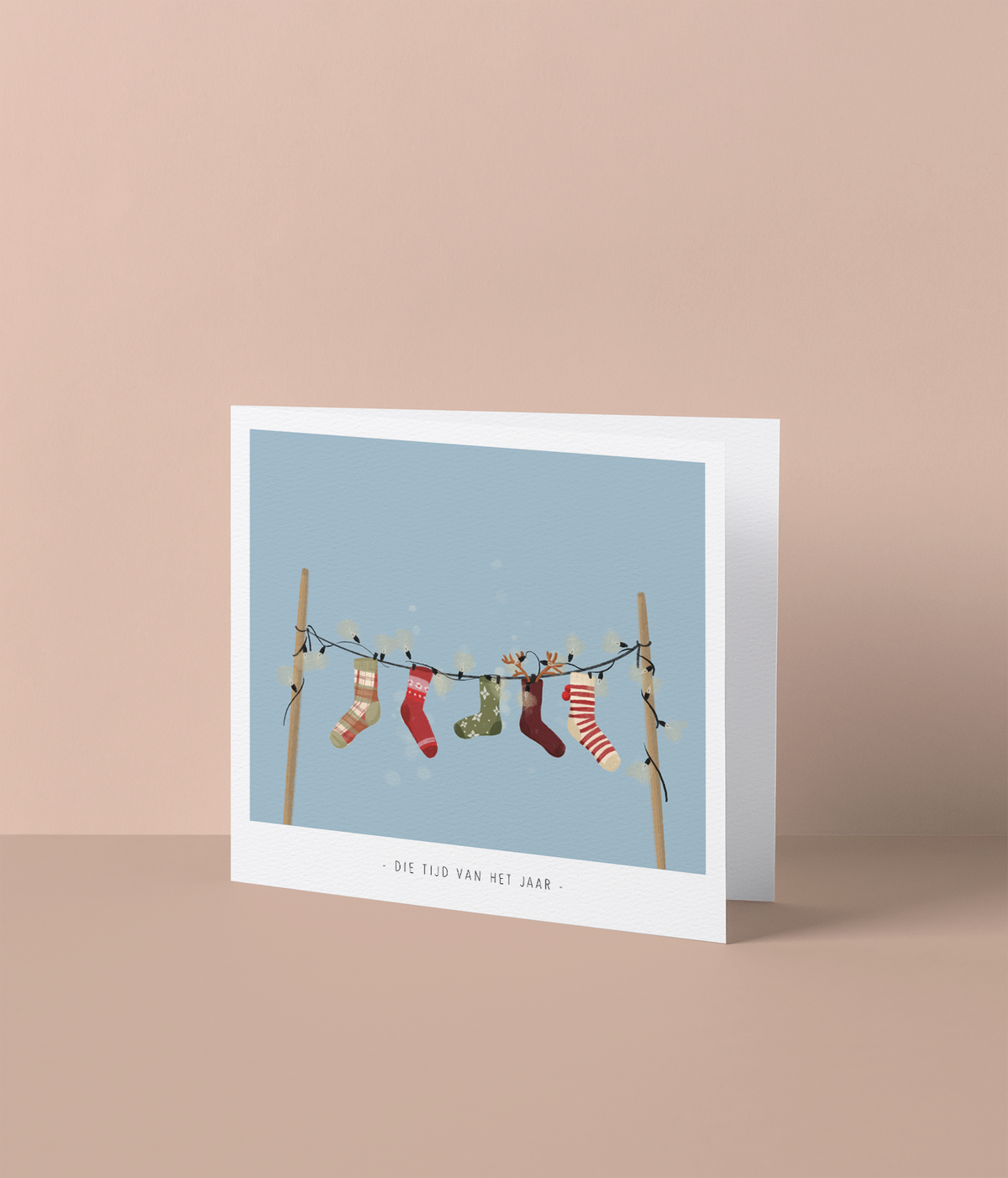 Kerstkaart met kerstsokken aan een lichtsnoer pastelblauwe achtergrond